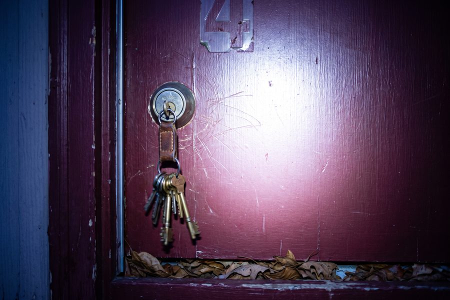 House keys left hanging in a front door lock, lit by a handheld work light at dusk