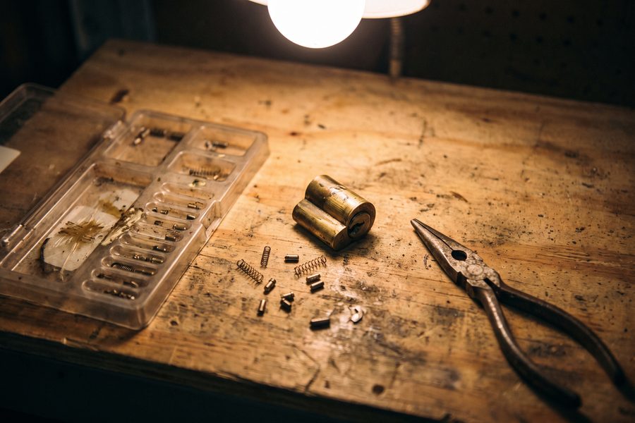 A brass door cylinder partly disassembled on a workbench with pins and a rekeying tray alongside